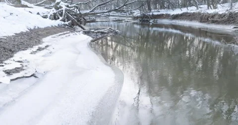 Low and slow float over a half frozen creek bisecting a Winter Forest Stock Footage 232558596