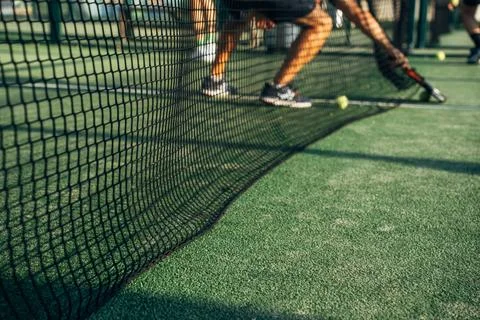 Low angle action shot of padel players through net, one reaching for ball Stock Photos