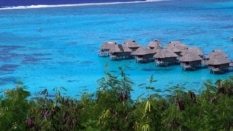 Low angle aerial glide view of overwater bungalow villas in lagoon in Moorea Stock Footage 122405407