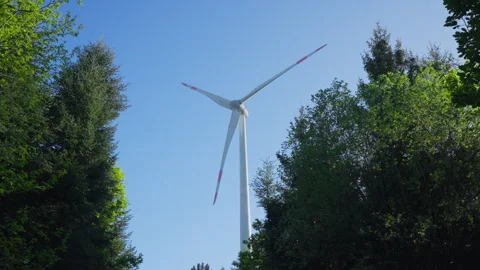 Low-Angle Aerial Shot of a Wind Turbine Tower Rising Above a Dense Forest 動画素材 338185456