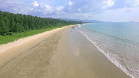 Low angle aerial view of a large, empty tropical beach surrounded by lush green Stock Footage 260994715