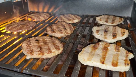 Low angle and close-up hamburgers and chicken burgers sizzle on hot grill. Stockbeeldmateriaal 337575099