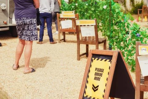 Low angle and selected focus on stand with queue message and people waiting Stock Photos