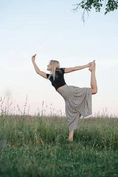 Low angle of balancing on one foot young blond woman exercising in a field Stock Photos