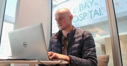 Low angle of bald male working on laptop in front of window Stock Footage 89462078