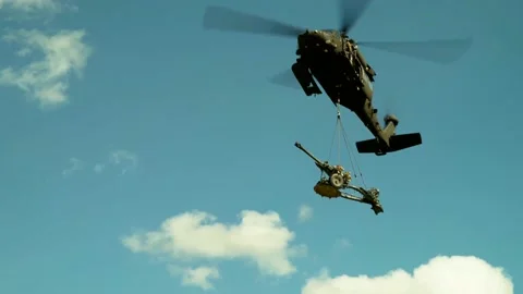 Low Angle of a Blackhawk Helicopter Transporting a Wheeled Artillery Gun Stock Footage 130361707
