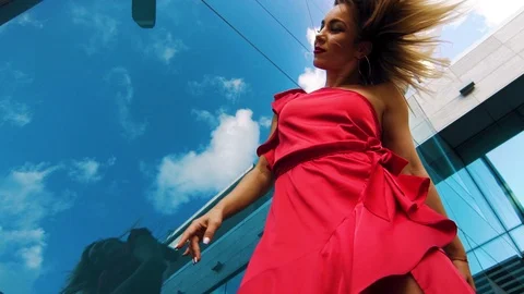 Low angle of blonde lady in red dancing against glass surface reflecting sky Stock Footage 112644669
