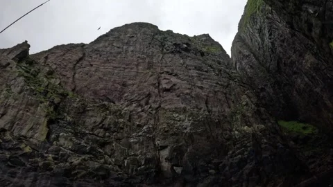 Low-angle boat POV looking up at towering basalt bird cliffs, Faroe Islands Stock Footage 339289143