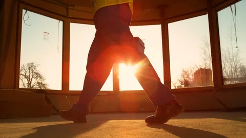 LOW ANGLE: Builder coming to work carries his toolbox across the room at sunrise Stock Footage 124692546