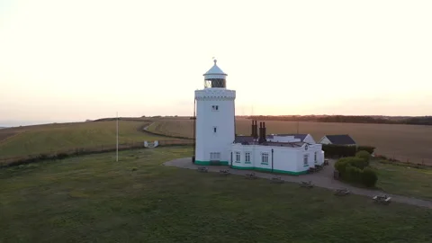 Low angle circling drone shot around a lighthouse at sunset with sun flare. 4k Stock Footage 147370000