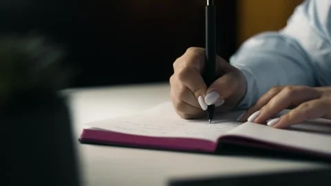Low angle close up of female hands writing in notebook in dark cozy room Stock Footage 343449418