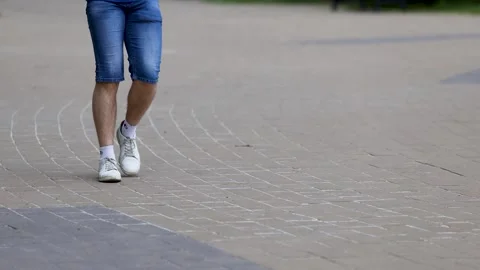 Low angle close-up of man legs in denim shorts and white sneakers walking on cit Stock Footage 335764795