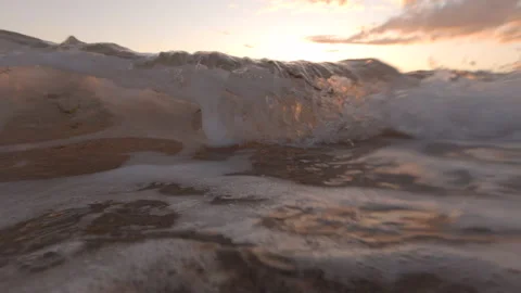 Low angle close up on sandy beach at sunset as waves wash over camera Stock Footage 132935631