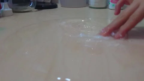 Low Angle Close Up Shot of Clear PVA Glue Base Puddle Spread Across Wooden Desk Stock Footage 342577101