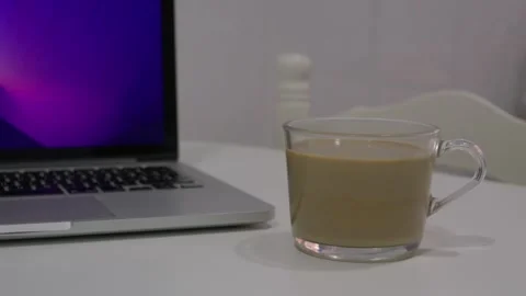 Low angle close up shot of a glass coffee mug resting near an open laptop on a Stock Footage 346505887