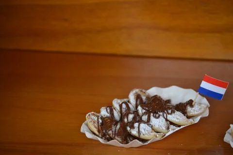 A low-angle, close-up shot of a small paper plate of Dutch poffertjes. The ti Stock Photos