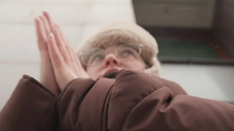 Low-angle close view of person in padded winter coat and furry hat warming hands Stock Footage 343524497