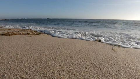 Low angle close up waves washing over sand on beach in summer Stock Footage 133979827