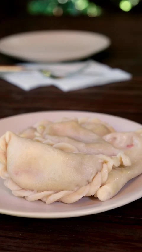 Low-angle closeup of boiled vareniki dumplings on pale round plate in rustic Stock Footage 345161775