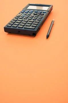 A low angle closeup of a graphing calculator and a tiny pen isolated on an or Stock Photos
