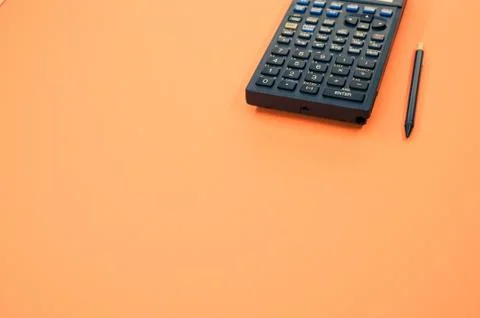 A low angle closeup of a graphing calculator and a tiny pen isolated on an or Stock Photos