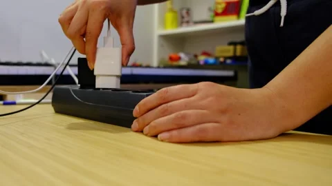 Low angle closeup of hands plugging a charger into a power strip on a wooden Stock Footage 329922174