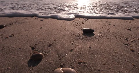 Low angle closeup of waves washing over sand on the beach with pebbles Stock Footage 135354441