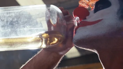 Low angle clown heavily drinking alcohol from glass bottle with lens flares. Stock Footage 91468393