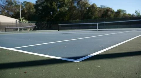 Low angle corner view of an empty tennis court with lamp post shadow Foto stock
