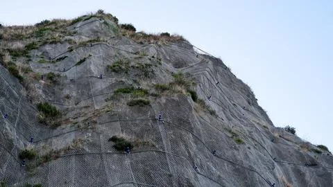 A low-angle detailed view of a steep rocky cliff face reinforced with a heavy Stock Photos