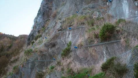 A low-angle detailed view of a steep rocky cliff face reinforced with a heavy Stock Photos