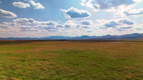 Low-angle drone flight over green fields to mountains 스톡 동영상 332727924