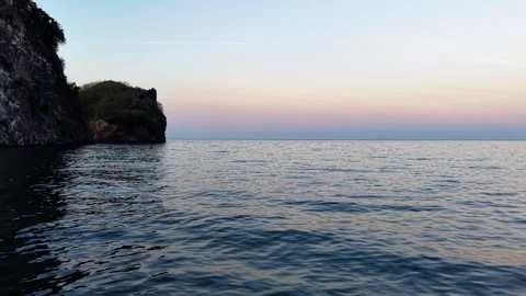 Low Angle Drone Flight Over Sea Surface Passing an Island at Sunset Stock Footage 334247688