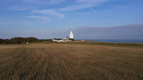 Low angle drone shot over a field with a lighthouse in the background. 4k Stock Footage 147367473