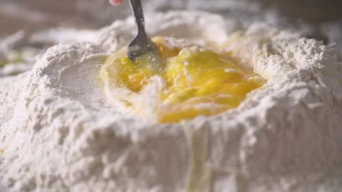 Low angle of eggs being scrambled in a flour well to make pasta shot in slow Stock Footage 171484846
