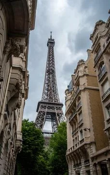 A low angle of the Eiffel Tower between buildings against a cloudy gray sky i Foto stock