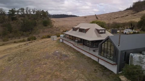 Low-angle flyover of a stone and glass villa in the Tasmanian mountains. Vídeo Stock 332542291