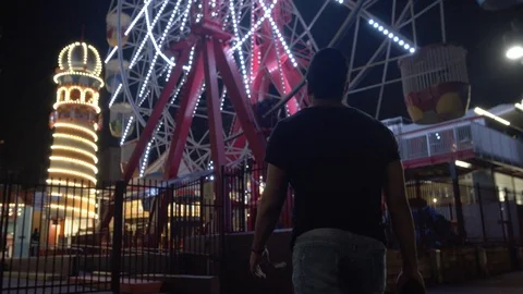 Low Angle Following Man Walking Towards Ferris Wheel in Theme Park Stock Footage 107900784