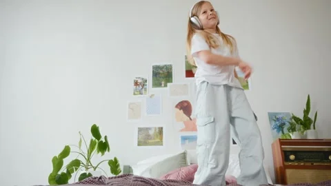 Low angle of girl dancing on bed in headphones Video stock 312288531