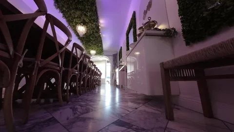 Low angle glide beside a long dining table in a purple-lit room Stock Footage 345564682
