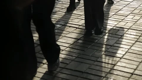 Low-angle glimpse of pedestrians walking across a sunlit brick sidewalk, their Vídeos de archivo 325671858