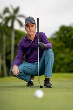 Low angle of a golfer kneeling down to guage the aim with blurry golf ball in Stockfoto's