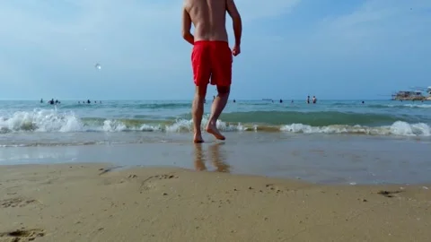 Low angle ground level pov of boy kicking red ball from beach to sea water Stock Footage 278966934