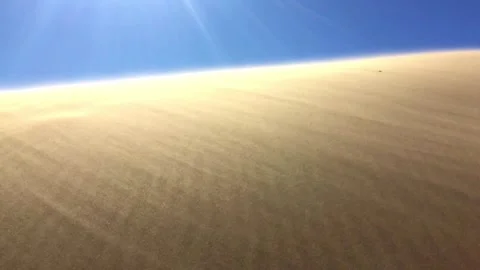 Low Angle Handheld Desert Sand Dunes Under Clear Blue Sky with Sun Flares 4K Stock Footage 327617942