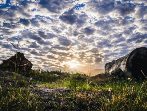 Low angle HDR of field with sun setting behind scattered clouds Stock Photos