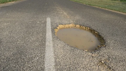 LOW ANGLE: Large gaping pothole filled with muddy water sticks out of empty road Stock Footage 87888818