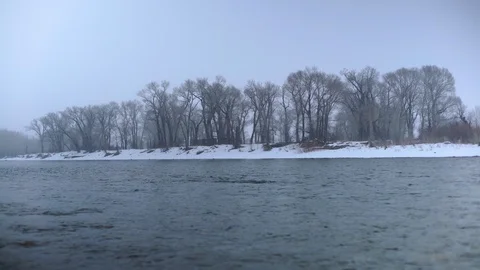 Low angle looking across Yellowstone River at trees in snow storm in winter Stock Footage 121064644