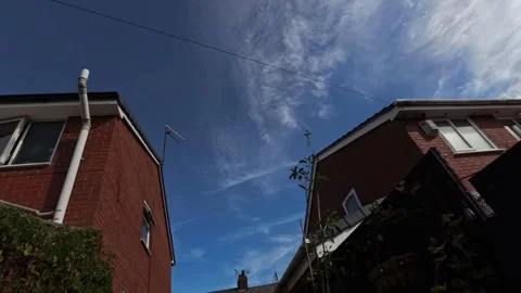 Low angle looking up between houses time lapse clouds passing across sunny blue Stock Footage 343080002