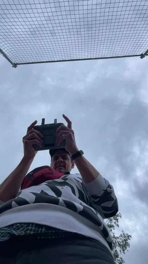 Low angle man holding remote controller beneath mesh net under overcast sky Видео 344584486