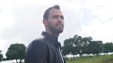 Low angle - man with jacket looks over - green fields and trees in BG Stock Footage 107277043